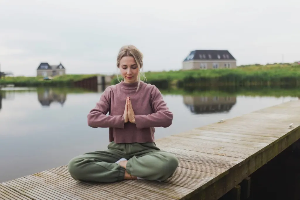 Woman practicing yoga meditation on deck by lake